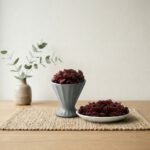 Premium dried cranberries by Oasis Dry Fruits in a grey pedestal cup and side plate, highlighting their vibrant ruby red color.