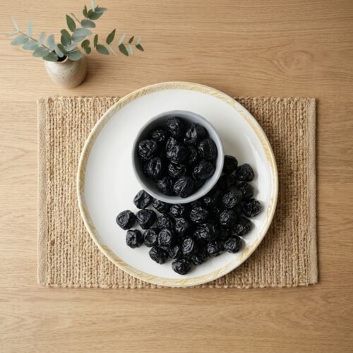 Top-down view of a plate of dried blackberry plums on a rustic jute mat, featuring the uniform size and high-fiber content of Oasis products.