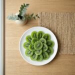 Dried green kiwi slices served in a white plate, ideal for a tangy-sweet healthy snack or as a vibrant addition to fruit platters.