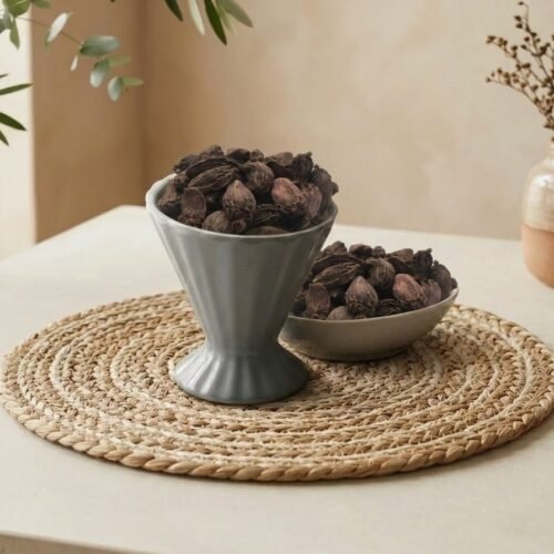 Whole smoky Black Cardamom pods served in a grey pedestal ceramic cup by Oasis Dry Fruits.