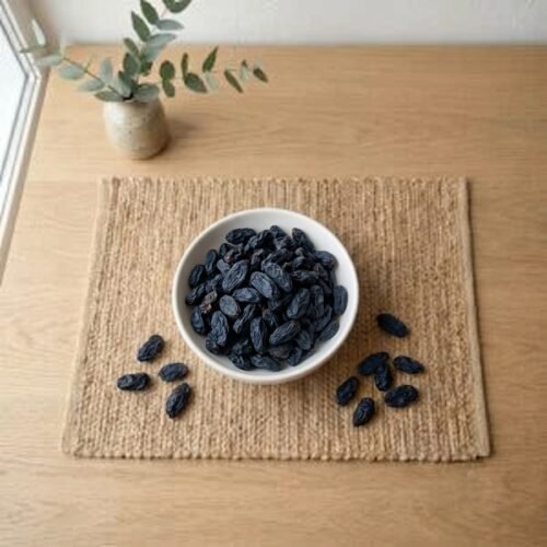 Top view flat lay of dried black raisins with seeds in a bowl by Oasis Dry Fruits.