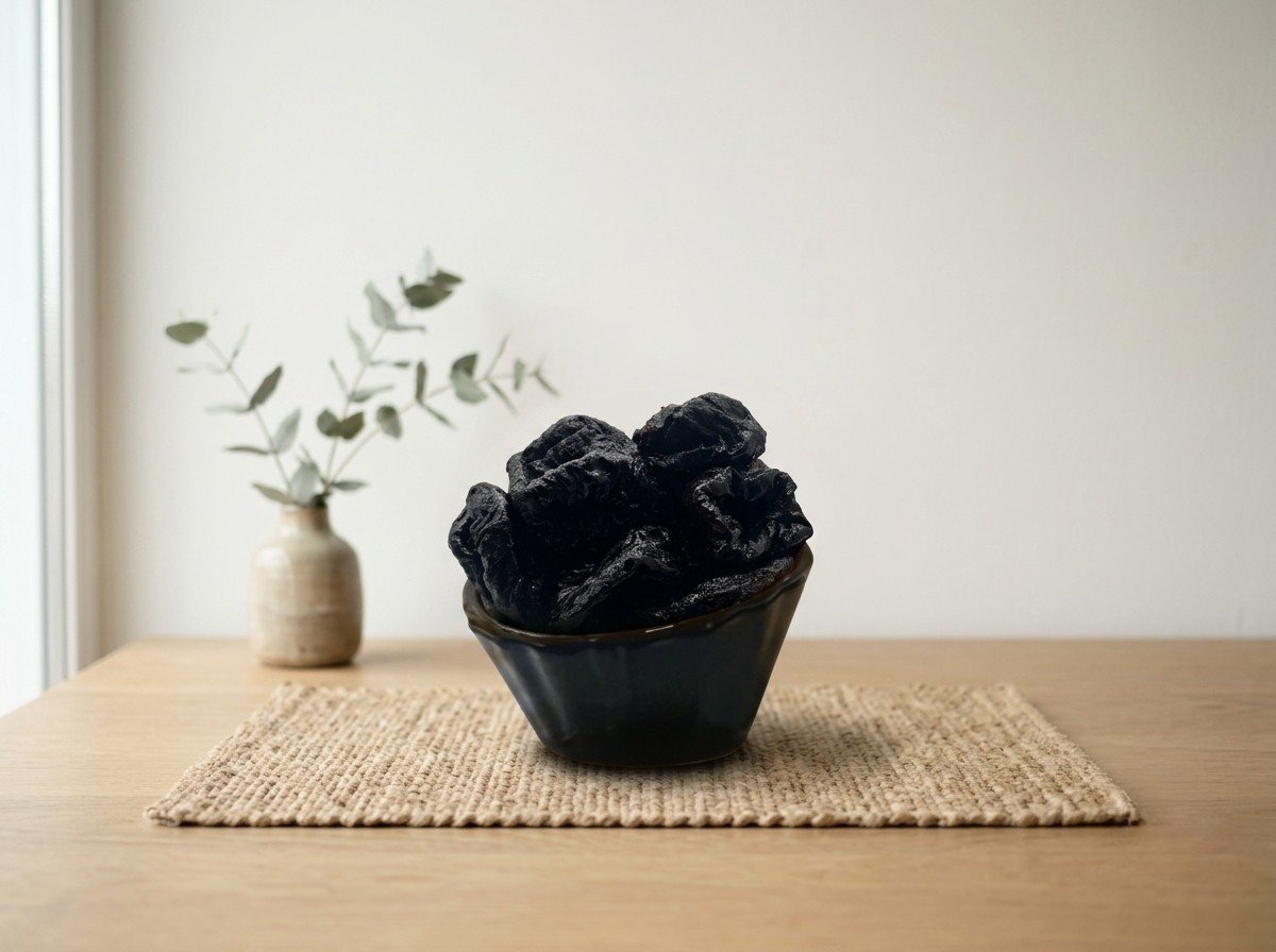 Side angle lifestyle shot of dried prunes in a dark bowl by Oasis Dry Fruits.