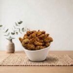 Side angle lifestyle shot of flavorful Flavoured Cashew (Tandoori) in a white bowl by Oasis Dry Fruits.