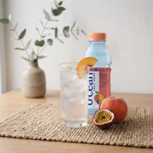 Glass of Ocean Fruit Drink Peach and Passion Fruit with ice, bottle behind
